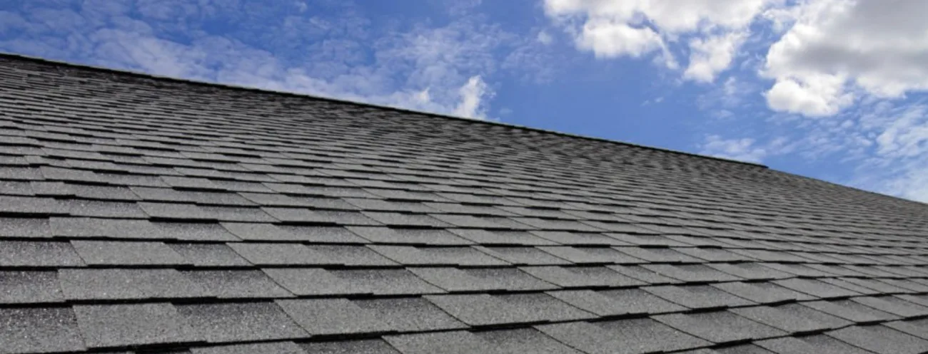 Dark asphalt shingle roof under a blue and cloudy Missouri sky