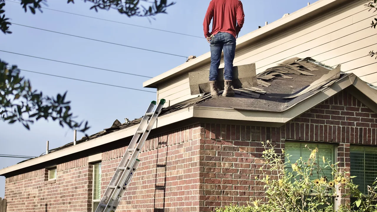 Roofer re-inspecting a storm-damaged roof to document an insurance claim